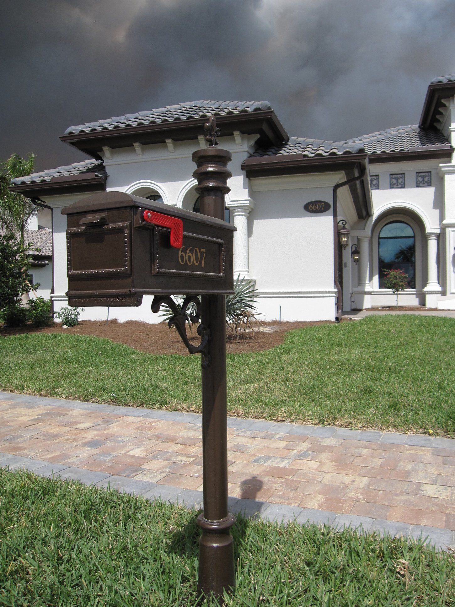 A mailbox in front of a white house with smoke coming out of the roof