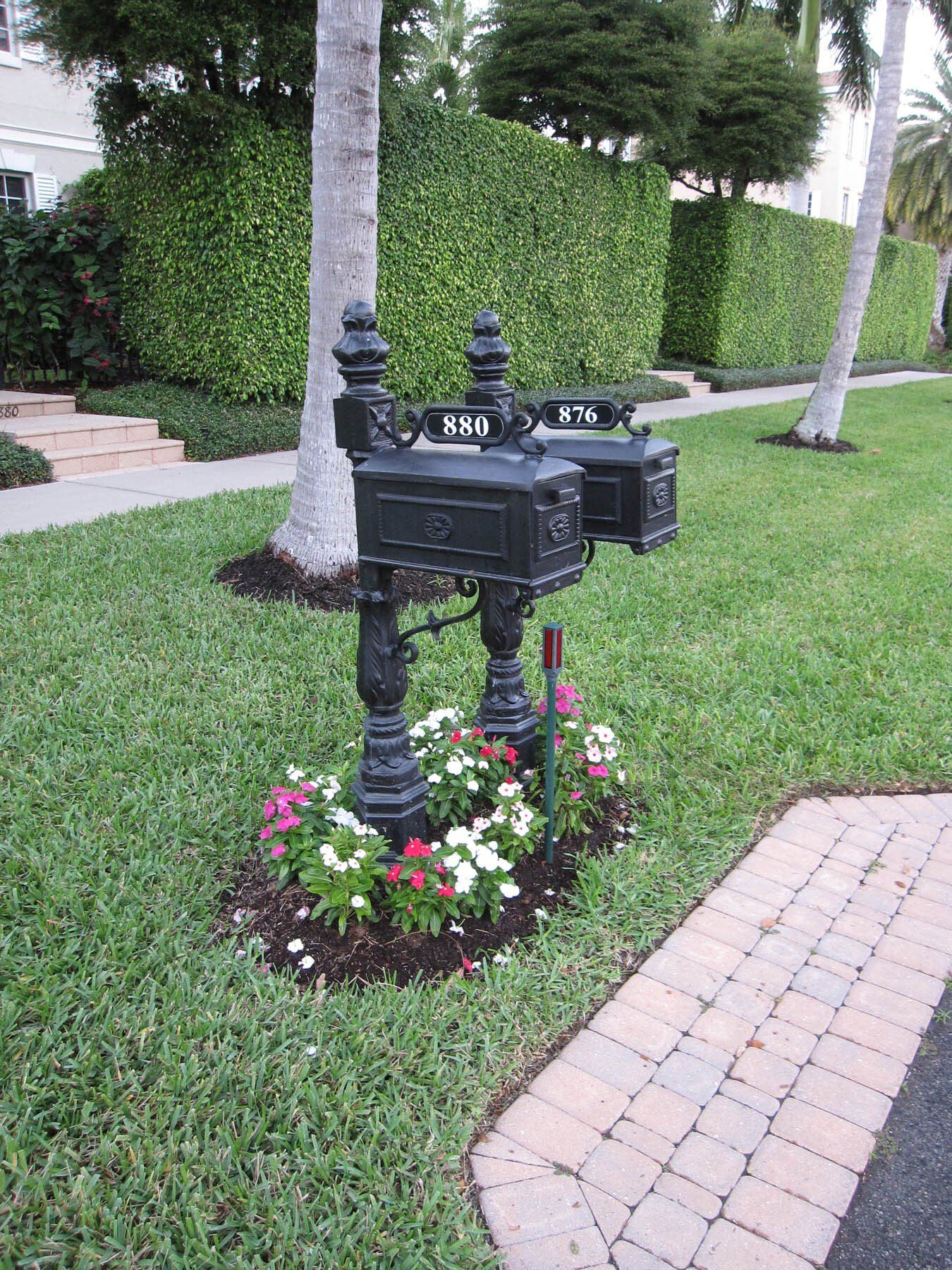 A black mailbox is sitting in the grass next to a brick walkway.