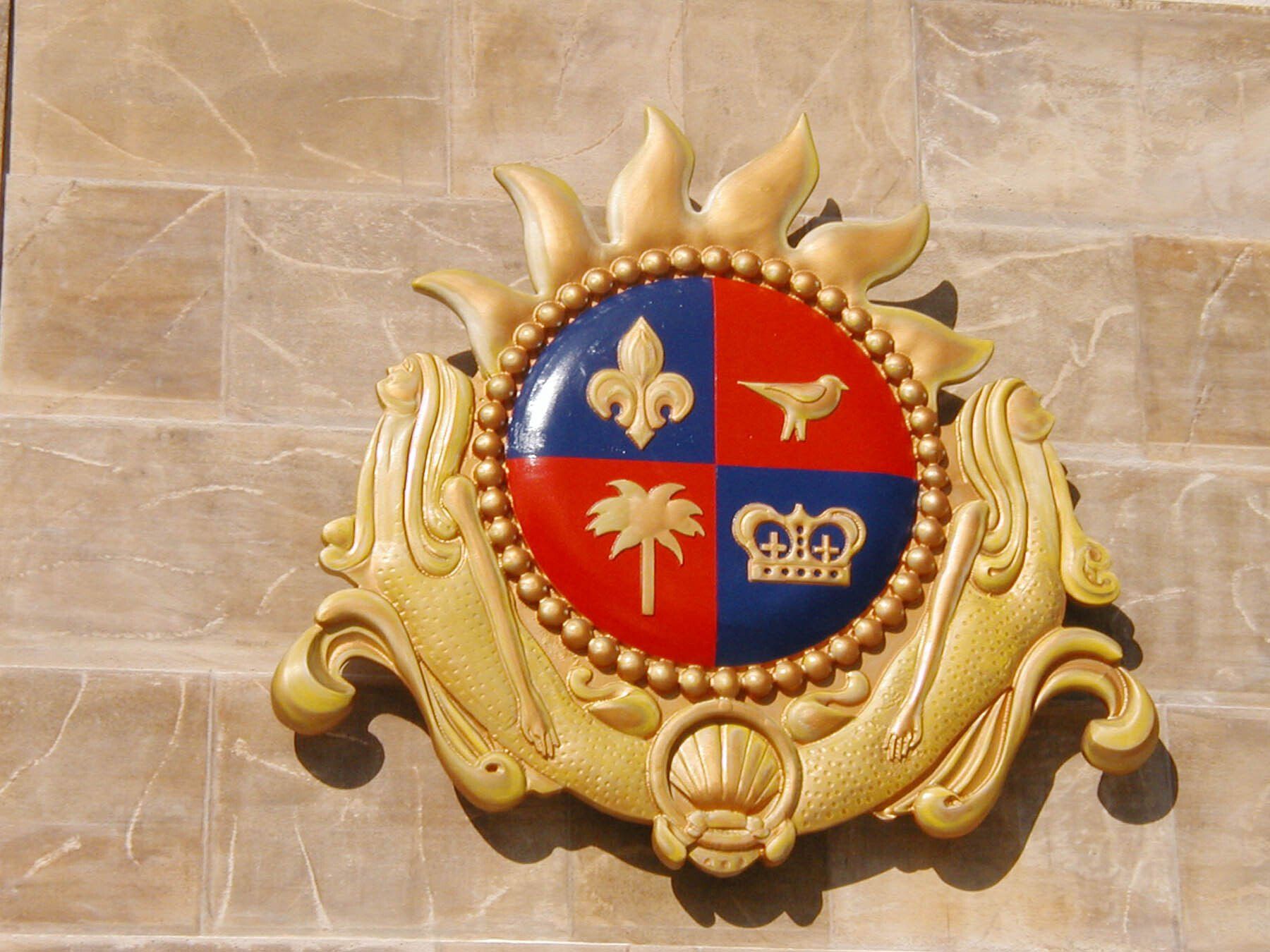 A gold and red coat of arms with palm trees and a crown