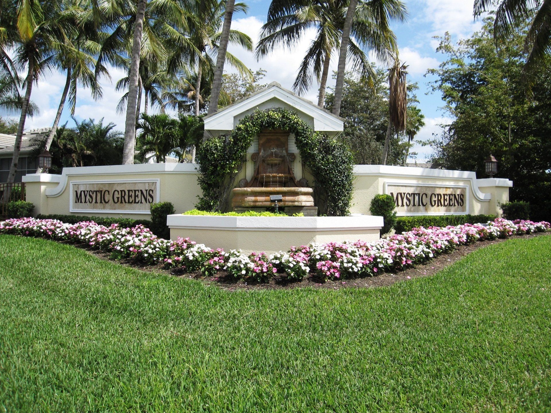 A sign for mystic greens is surrounded by flowers and palm trees
