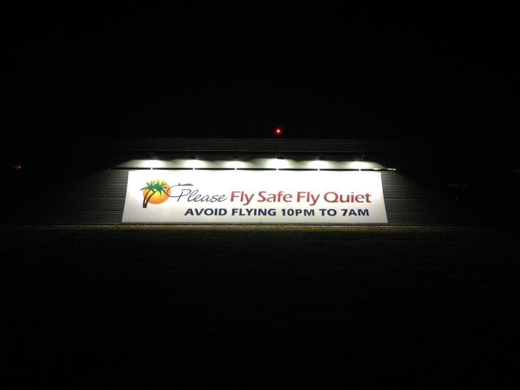 A sign that says please fly safe fly quiet is lit up at night