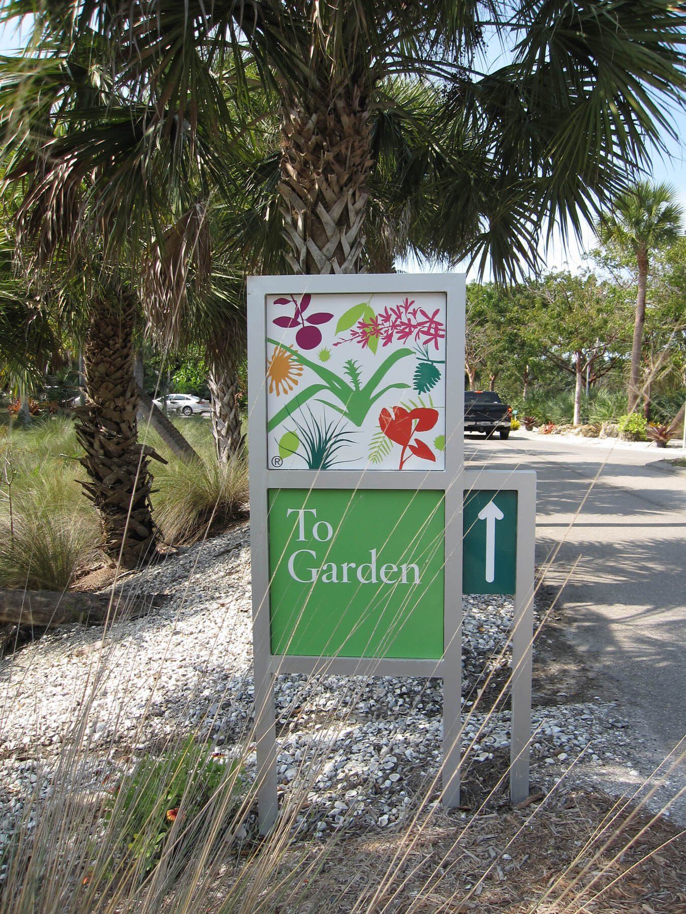 A sign for a garden with a palm tree in the background