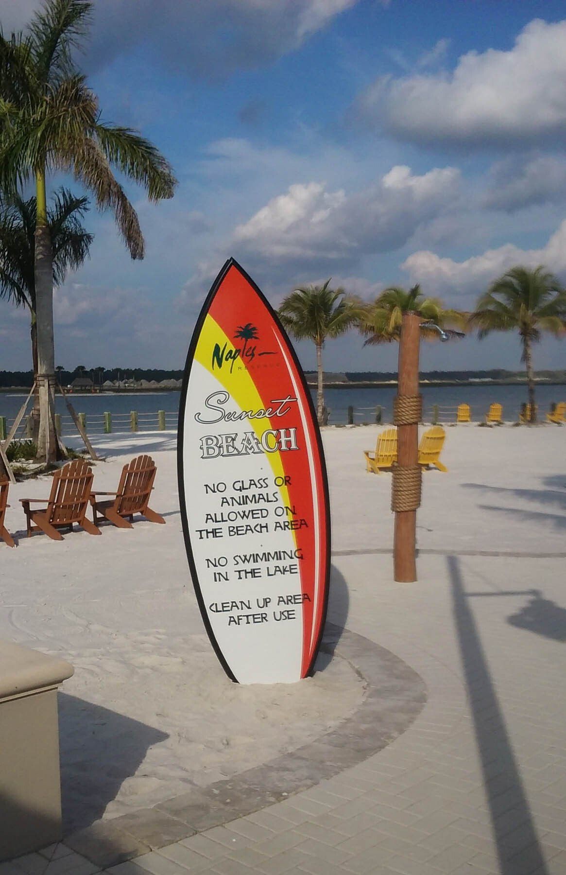 A large surfboard on a sandy beach with palm trees in the background