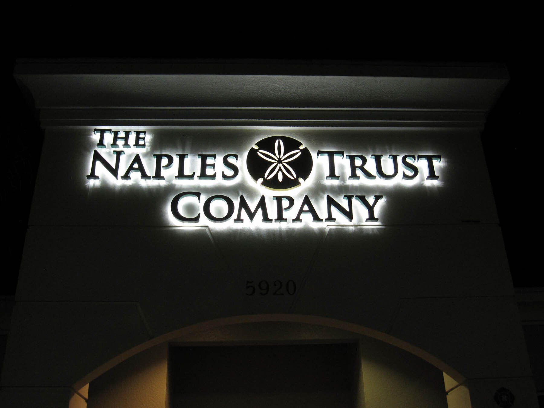 A sign for the naples trust company is lit up at night