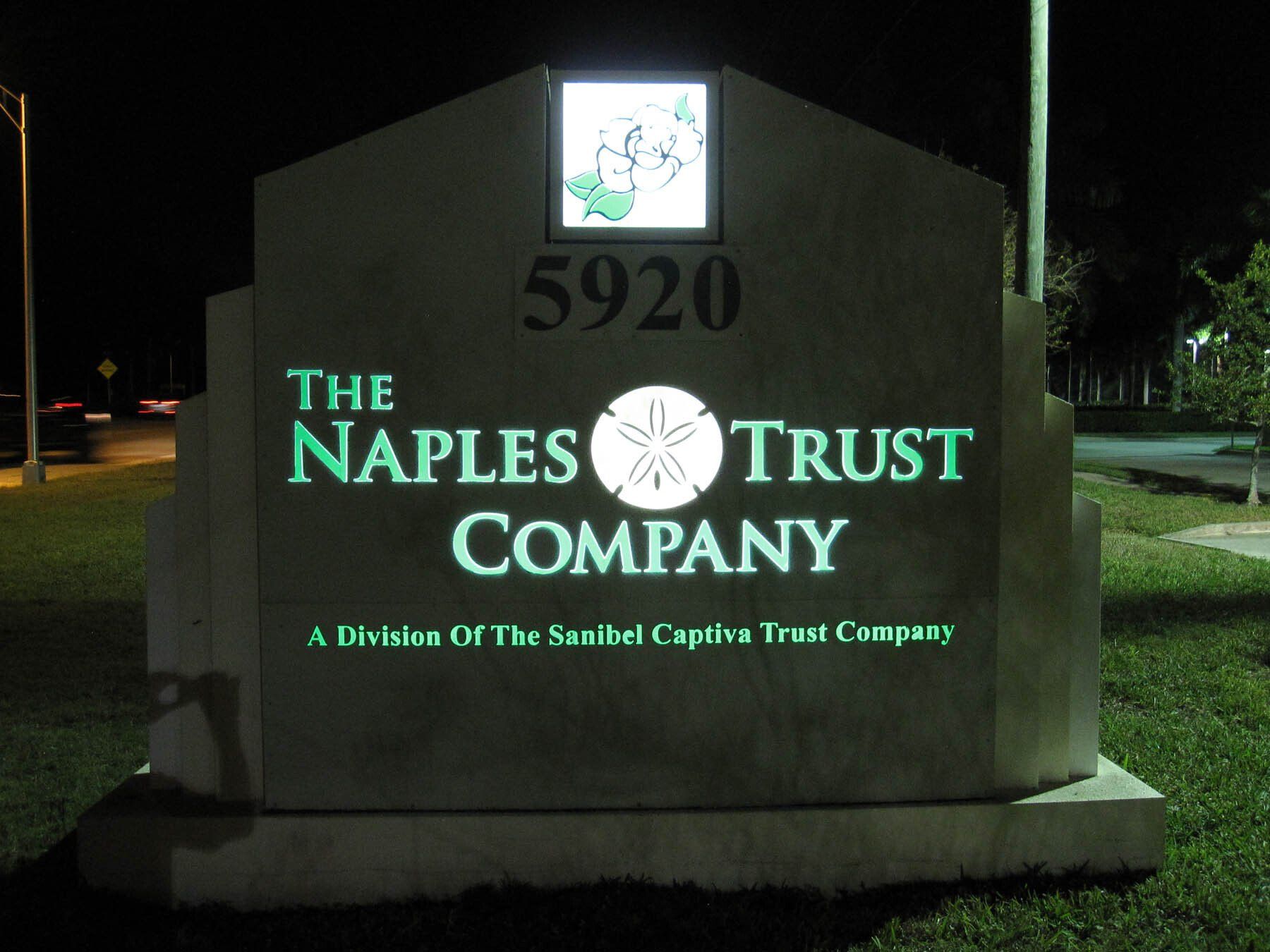 A sign for the naples trust company is lit up at night