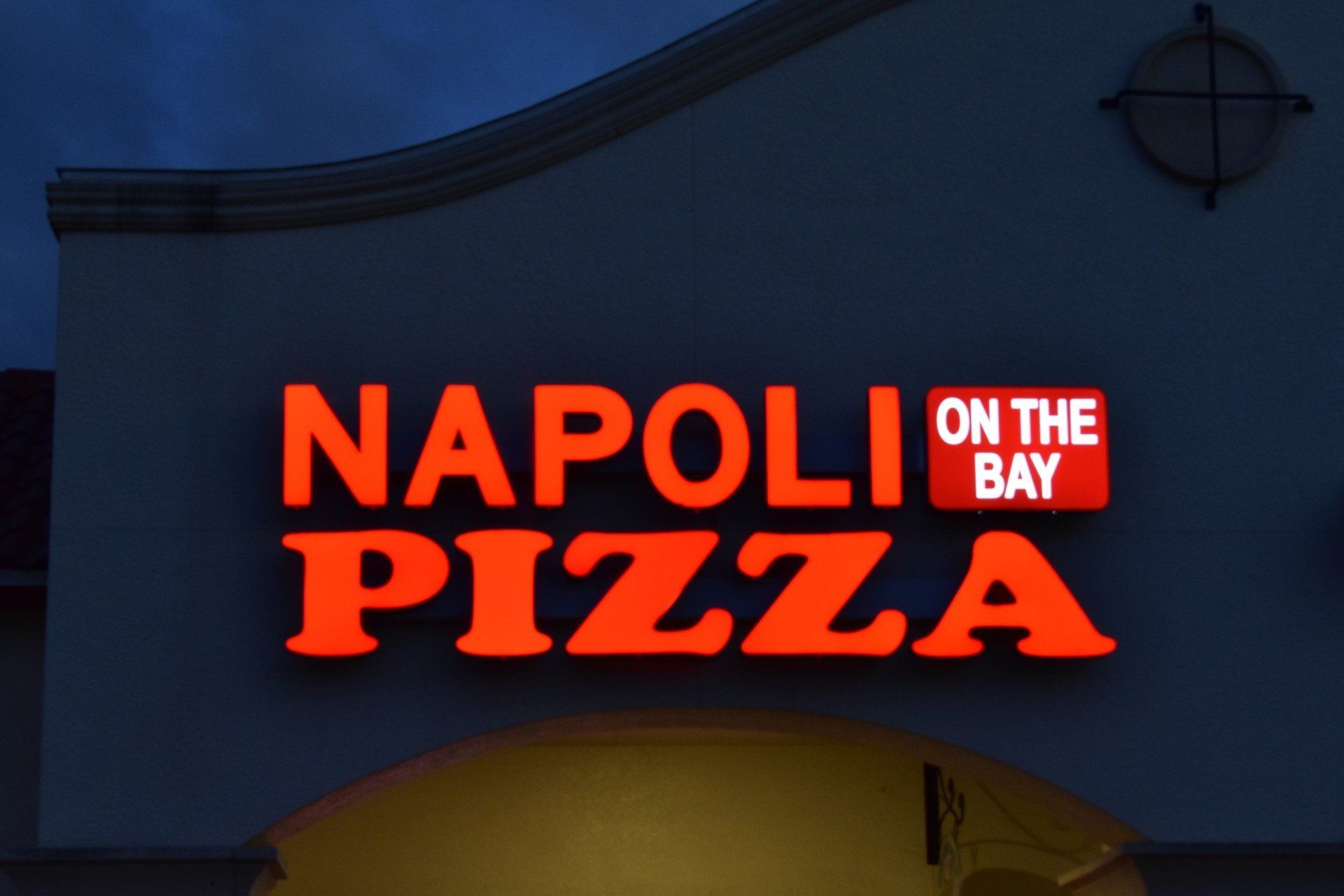 A sign for napoli on the bay pizza is lit up at night