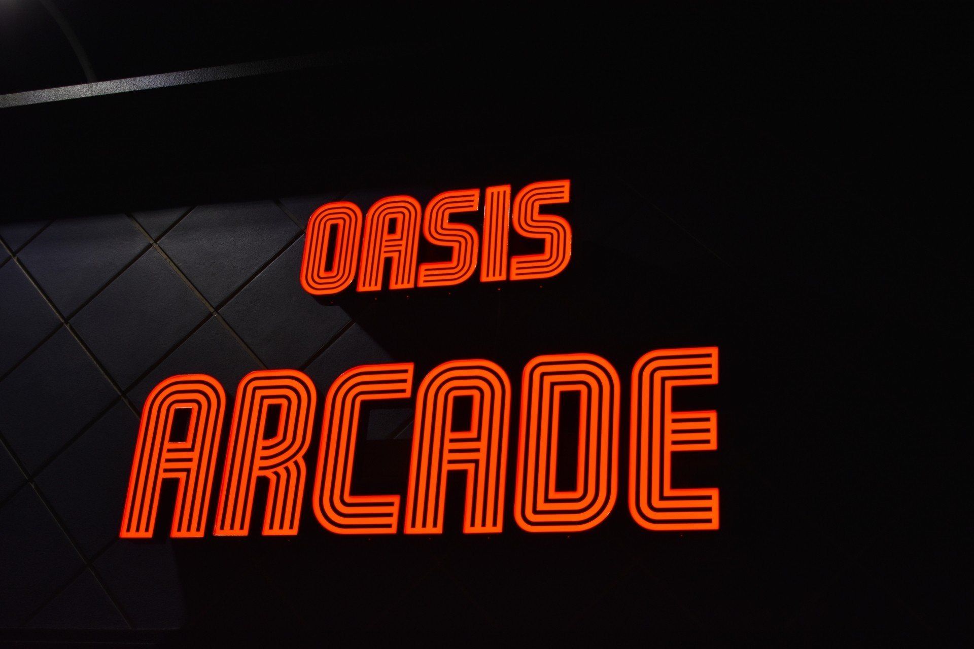 A lit channel letter sign with red text for Oasis Arcade at night, stylized to look like an old neon arcade sign.