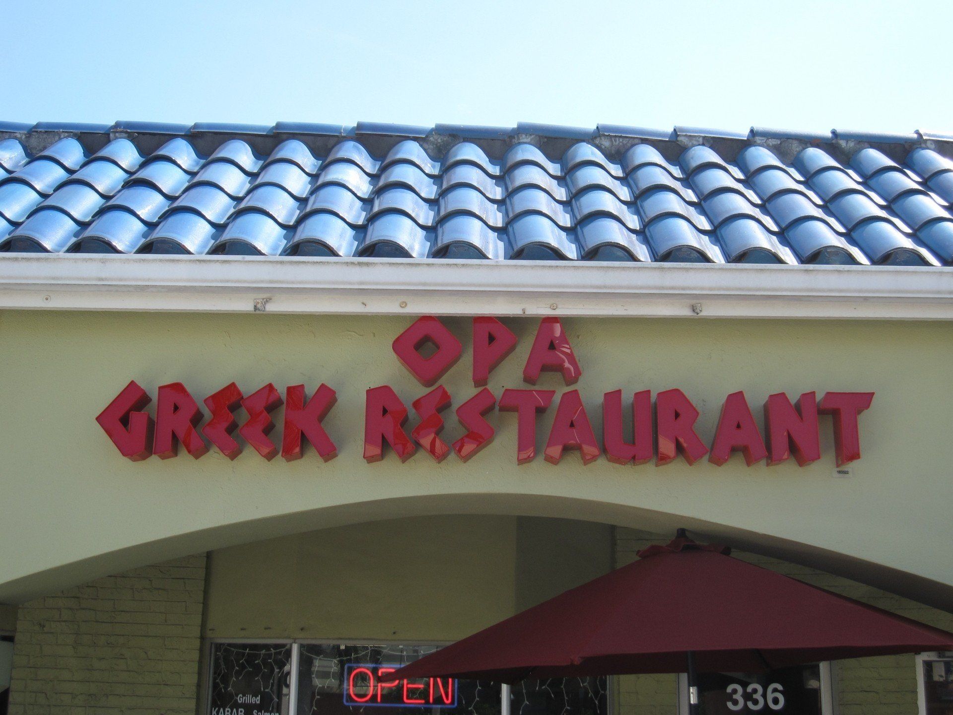 A greek restaurant with a red umbrella in front of it