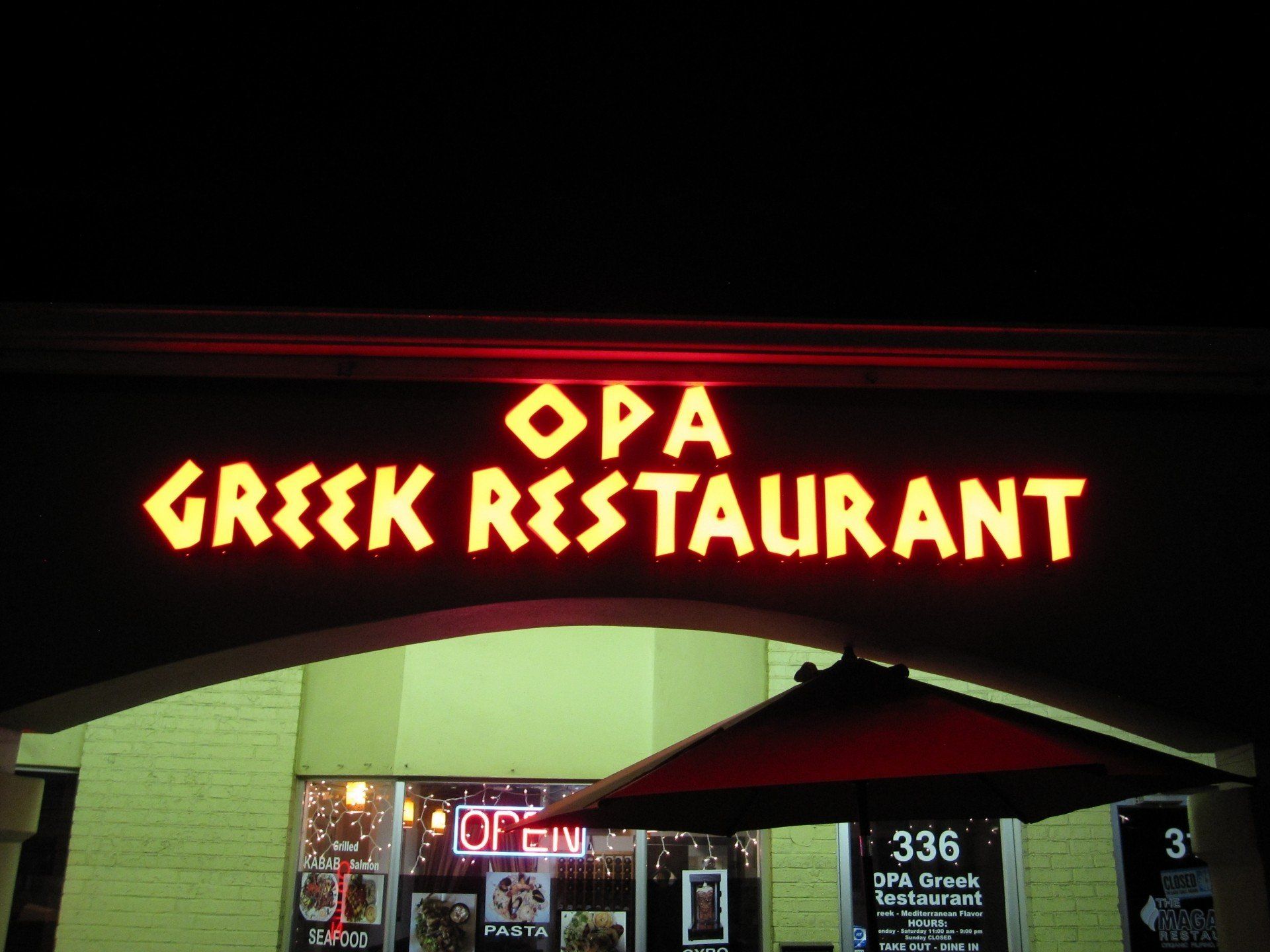 A sign for opa greek restaurant is lit up at night