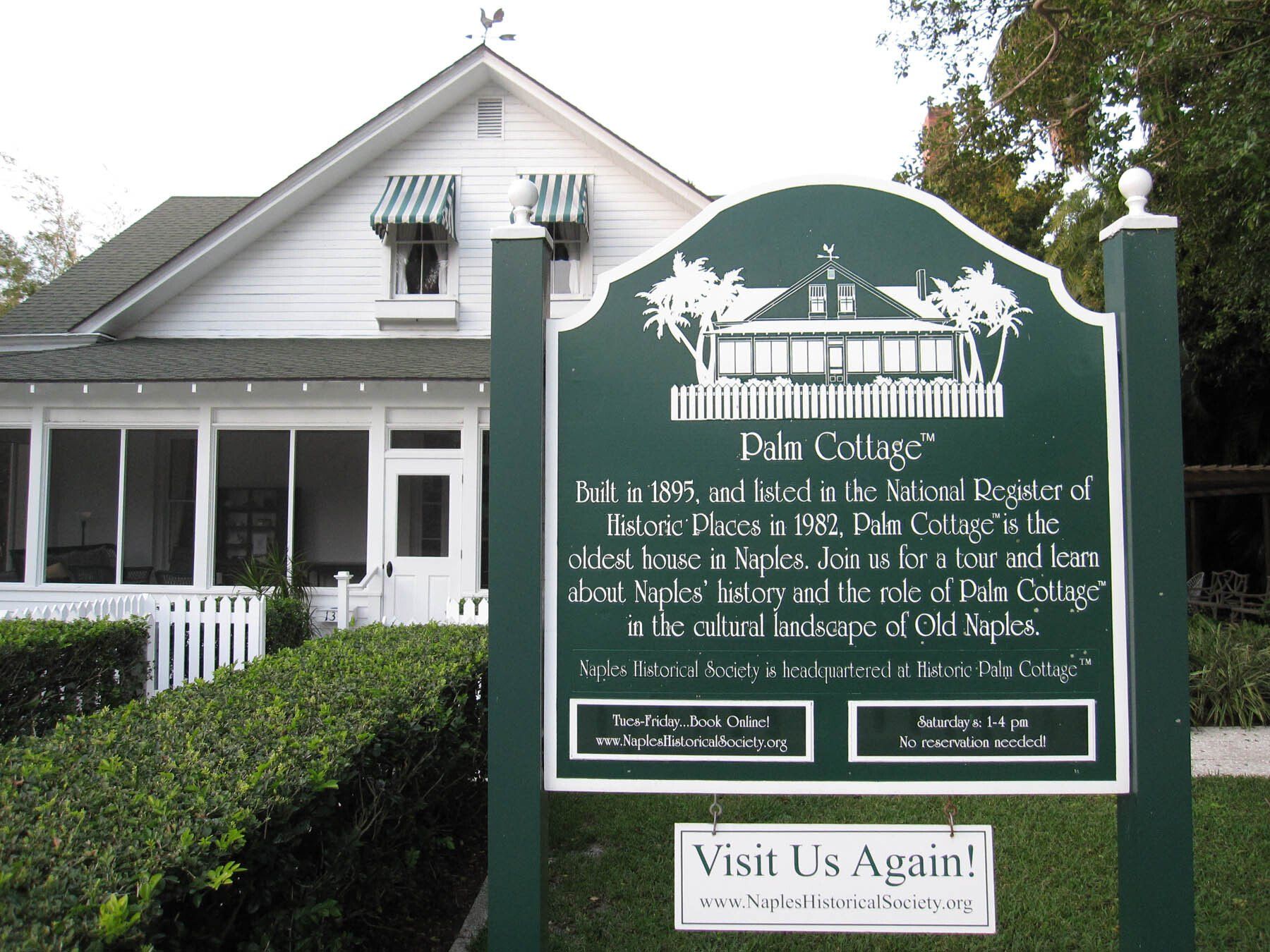 A palm cottage sign in front of a white house
