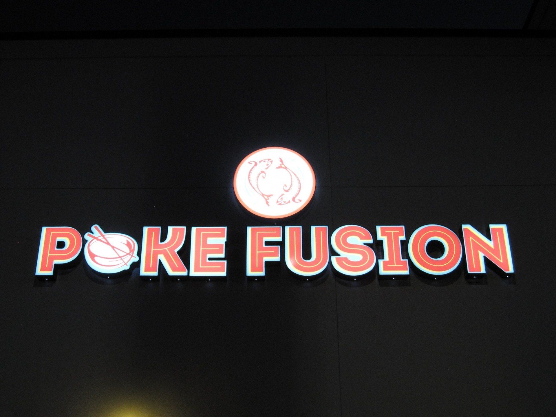 A sign for poke fusion is lit up at night