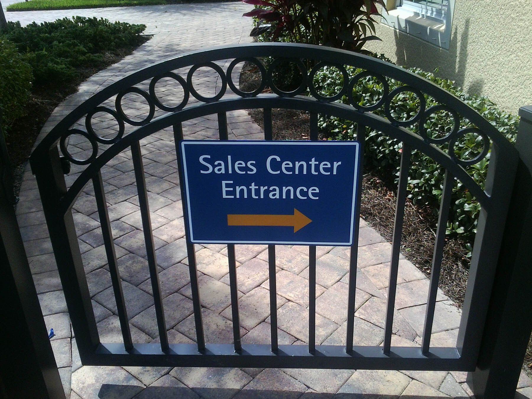 A gate with a blue sign that says sales center entrance