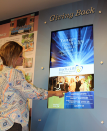 A woman is touching a screen that says giving back