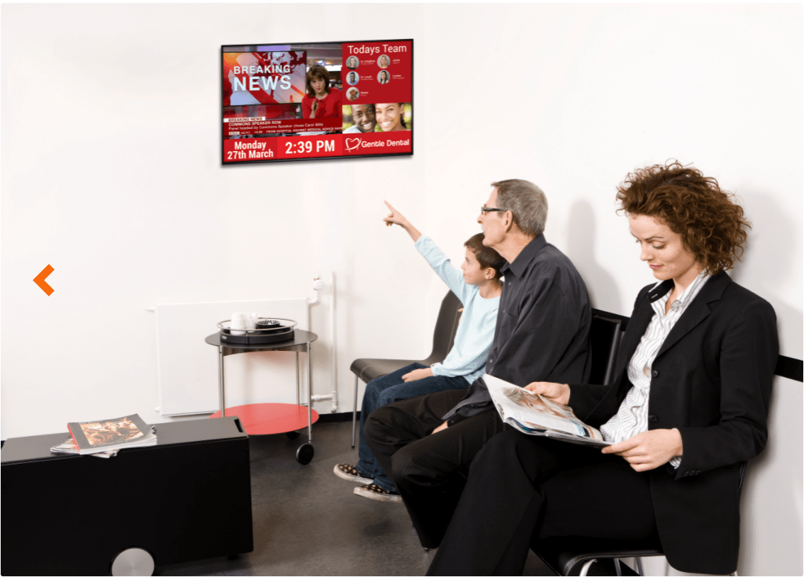 A group of people are sitting in a waiting room watching a television.