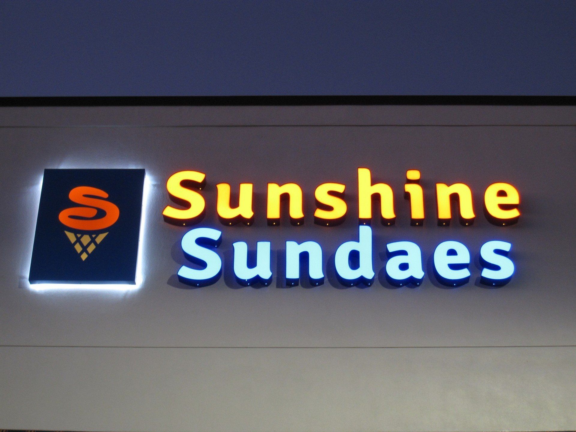 A sign for sunshine sundaes is lit up at night