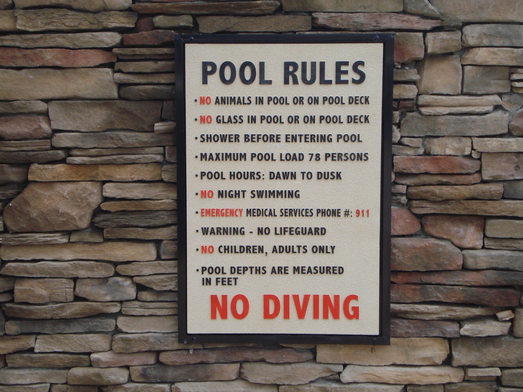 A sign on a stone wall that says pool rules and no diving