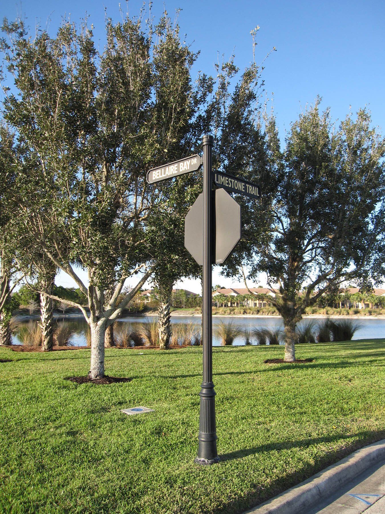 A street sign in a park with trees and a lake in the background