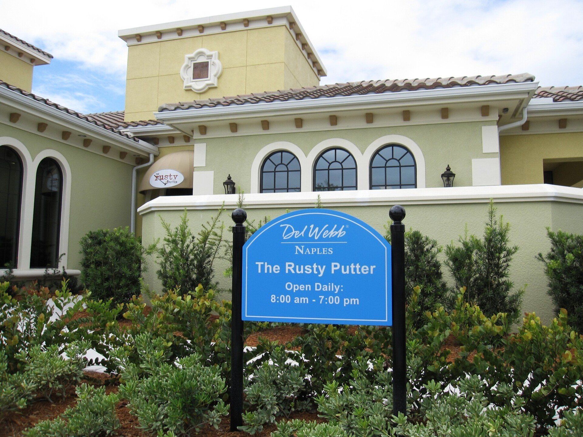 A blue sign in front of a building that says the rusty putter