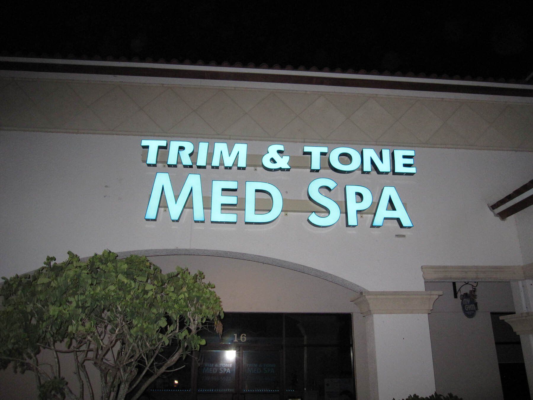 A trim and tone med spa sign is lit up at night