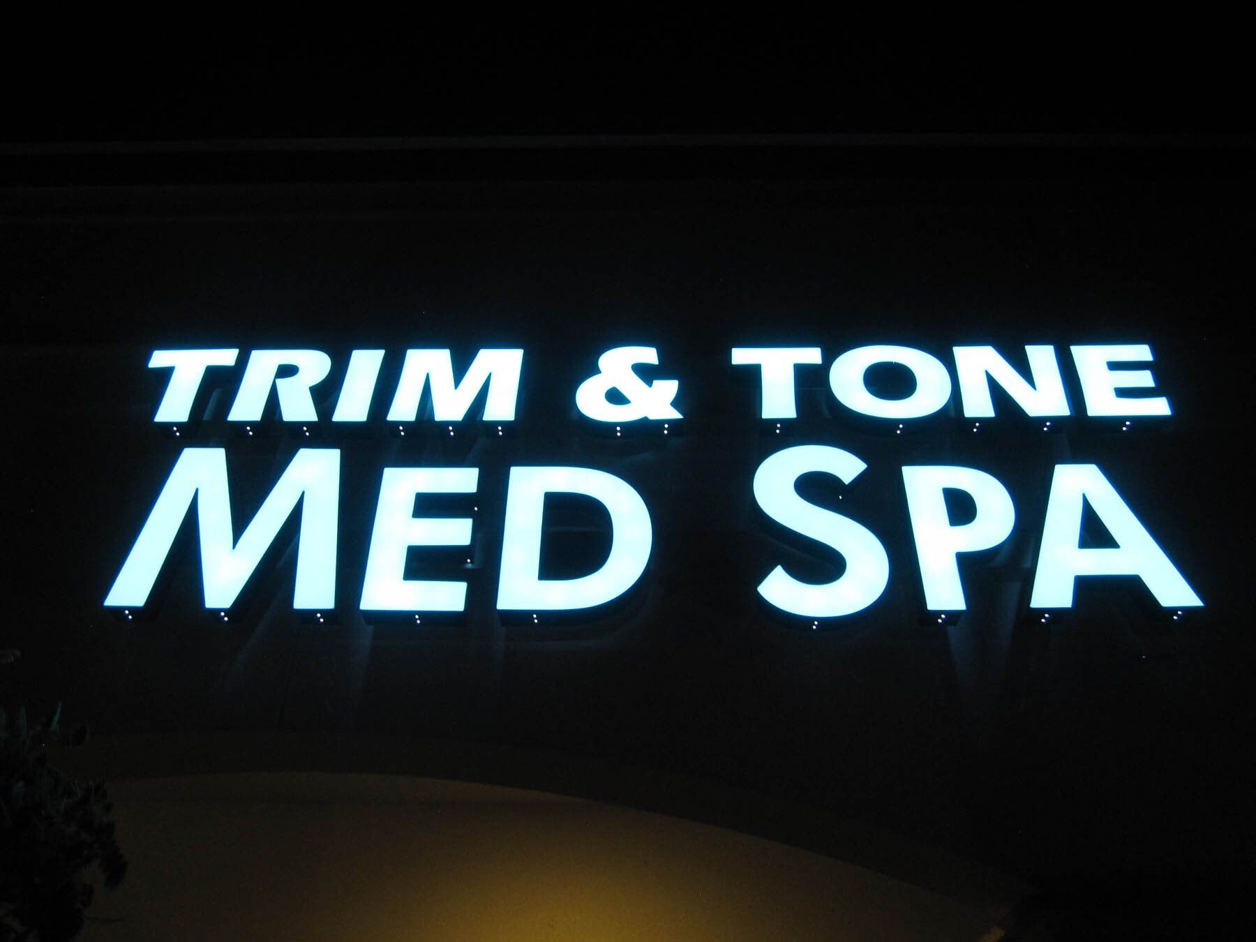 A sign for trim and tone med spa is lit up at night