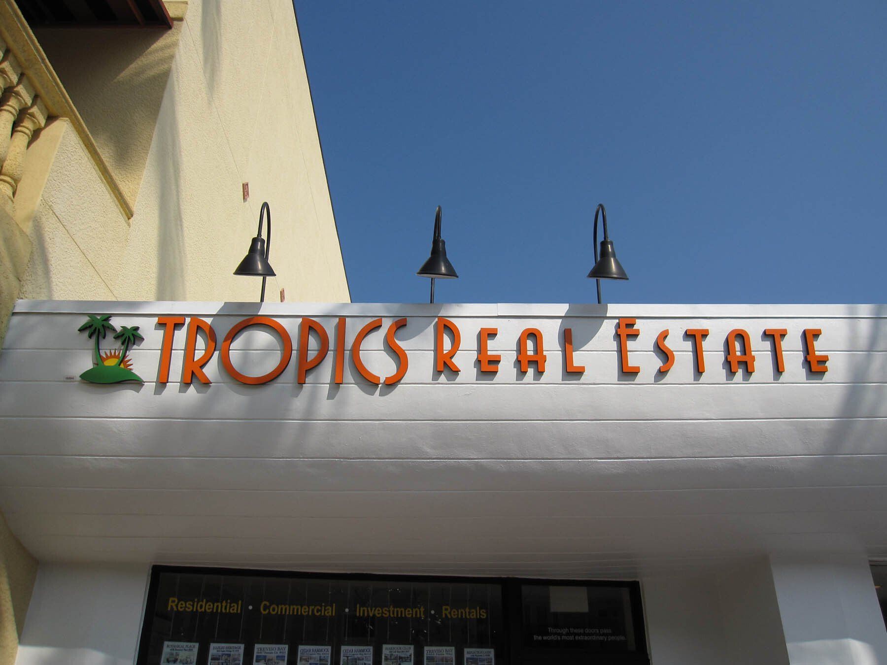 A sign for tropics real estate hangs from the side of a building