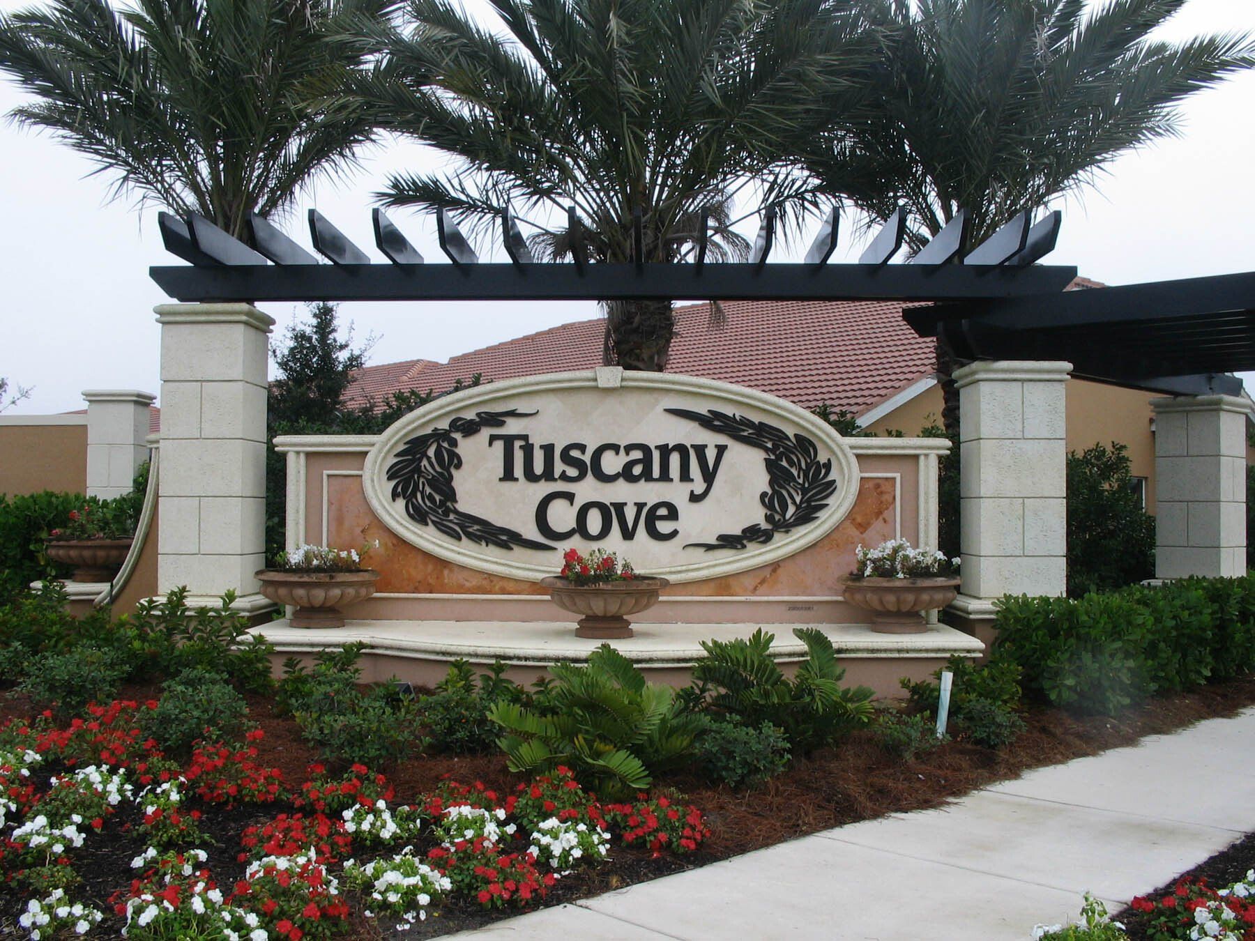 A sign for tuscany cove is surrounded by flowers and palm trees