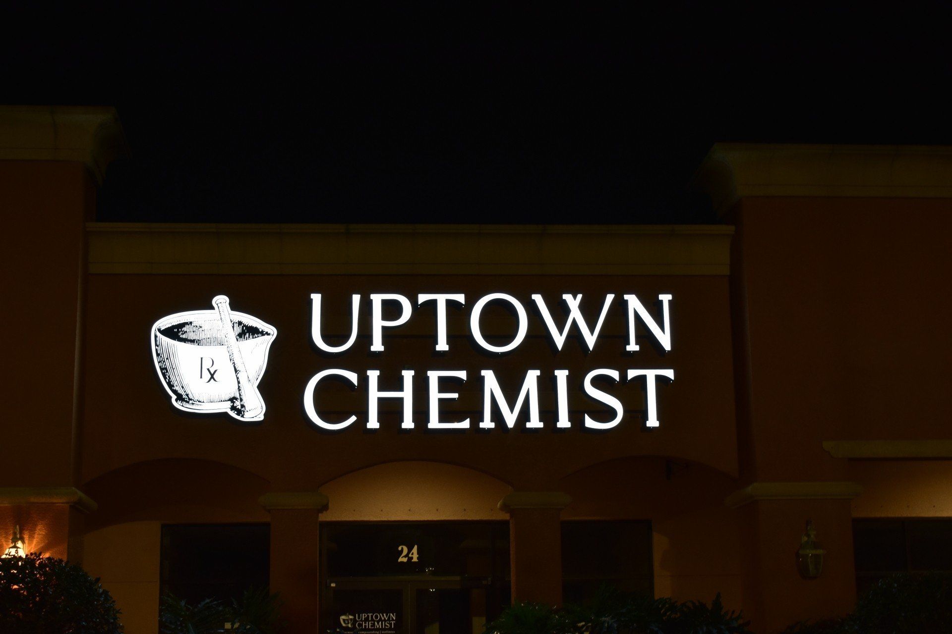 A sign for uptown chemist is lit up at night.