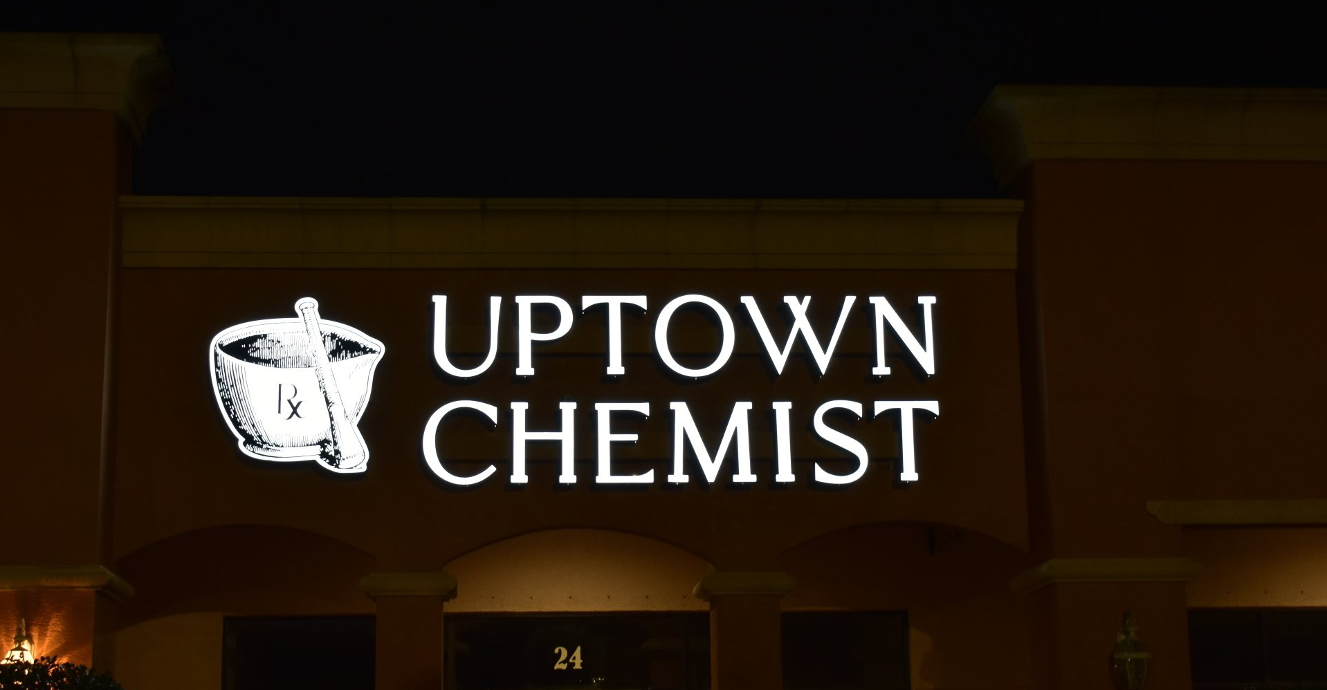 A sign for uptown chemist is lit up at night.