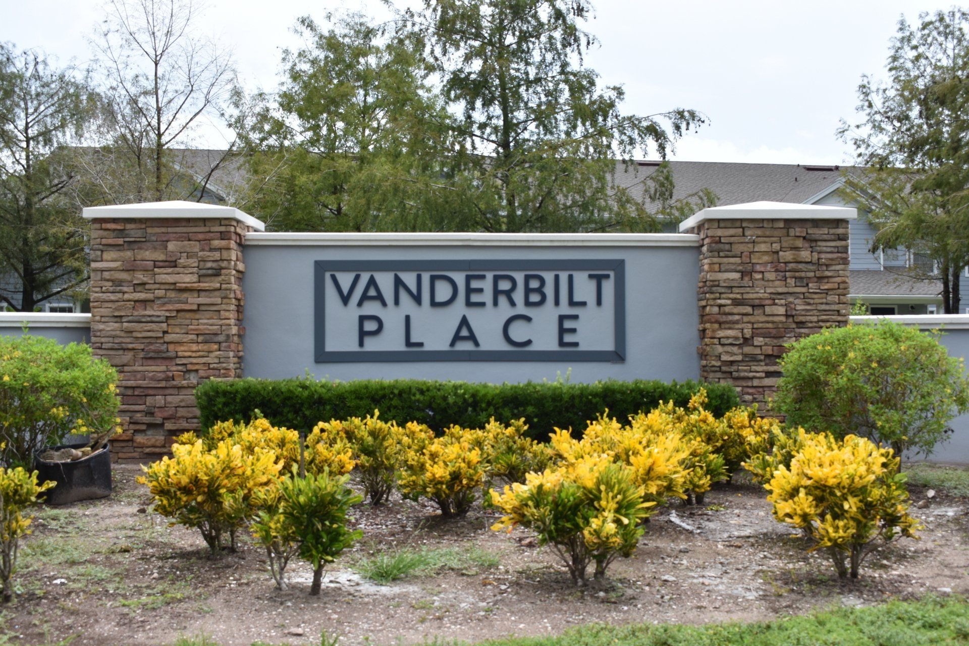 A sign for vanderbilt place is surrounded by flowers and bushes.