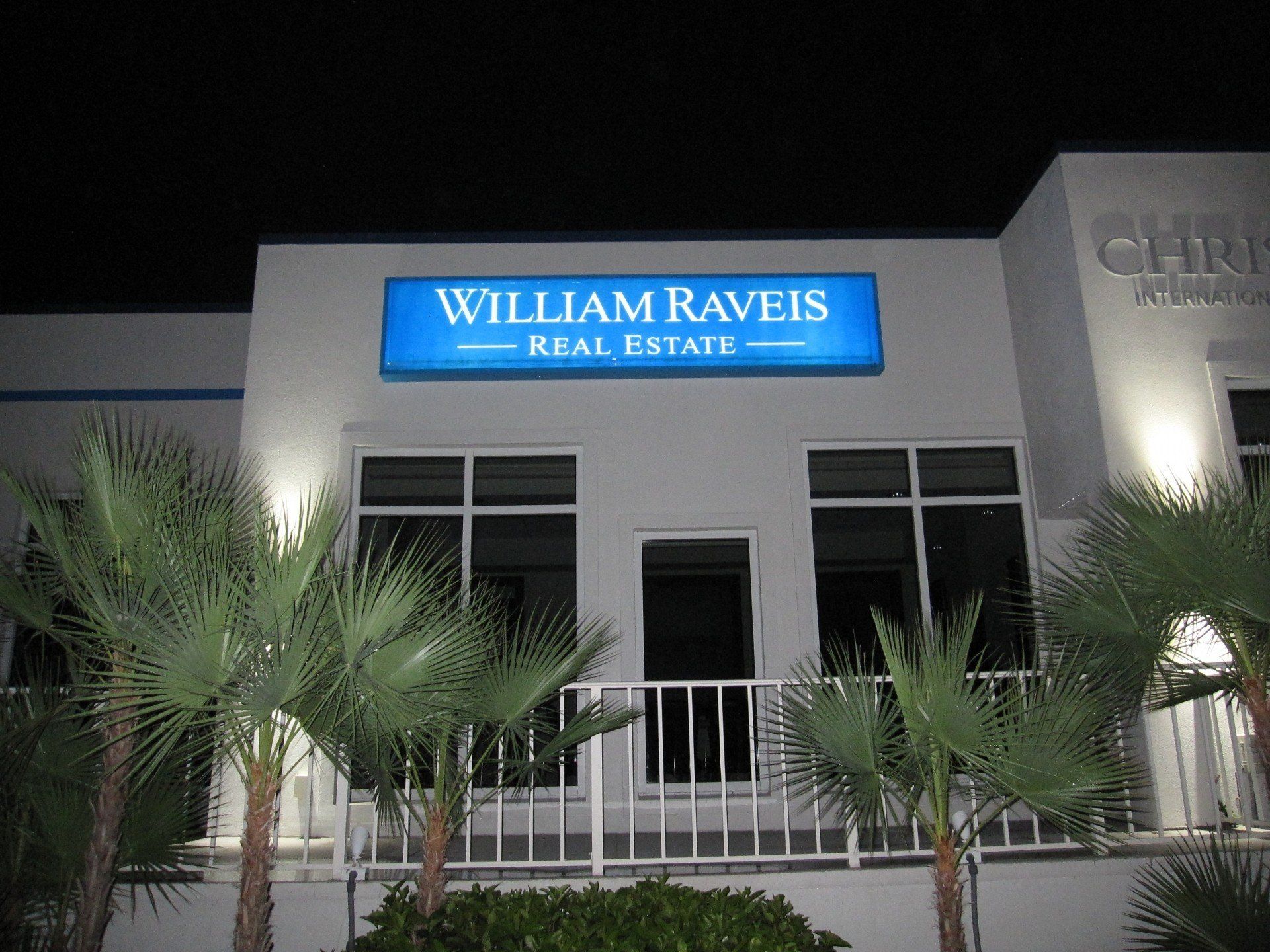 A white building with a blue sign that says william raveis real estate