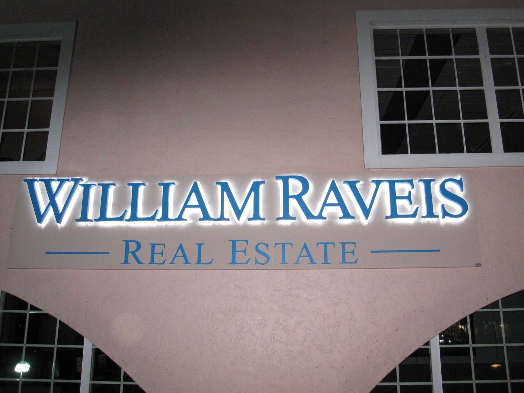 A sign for william raveis real estate is lit up at night