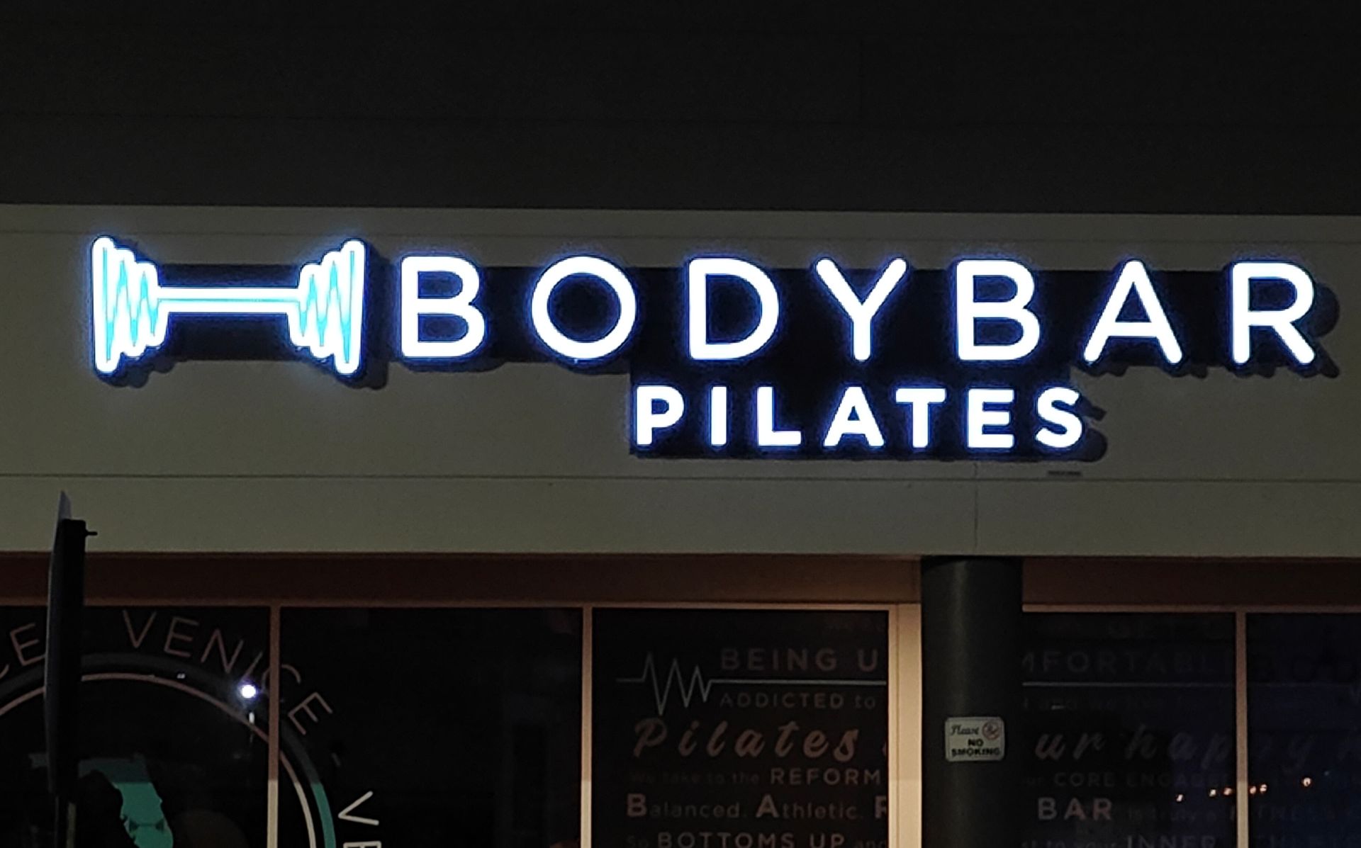 A body bar pilates sign is lit up at night