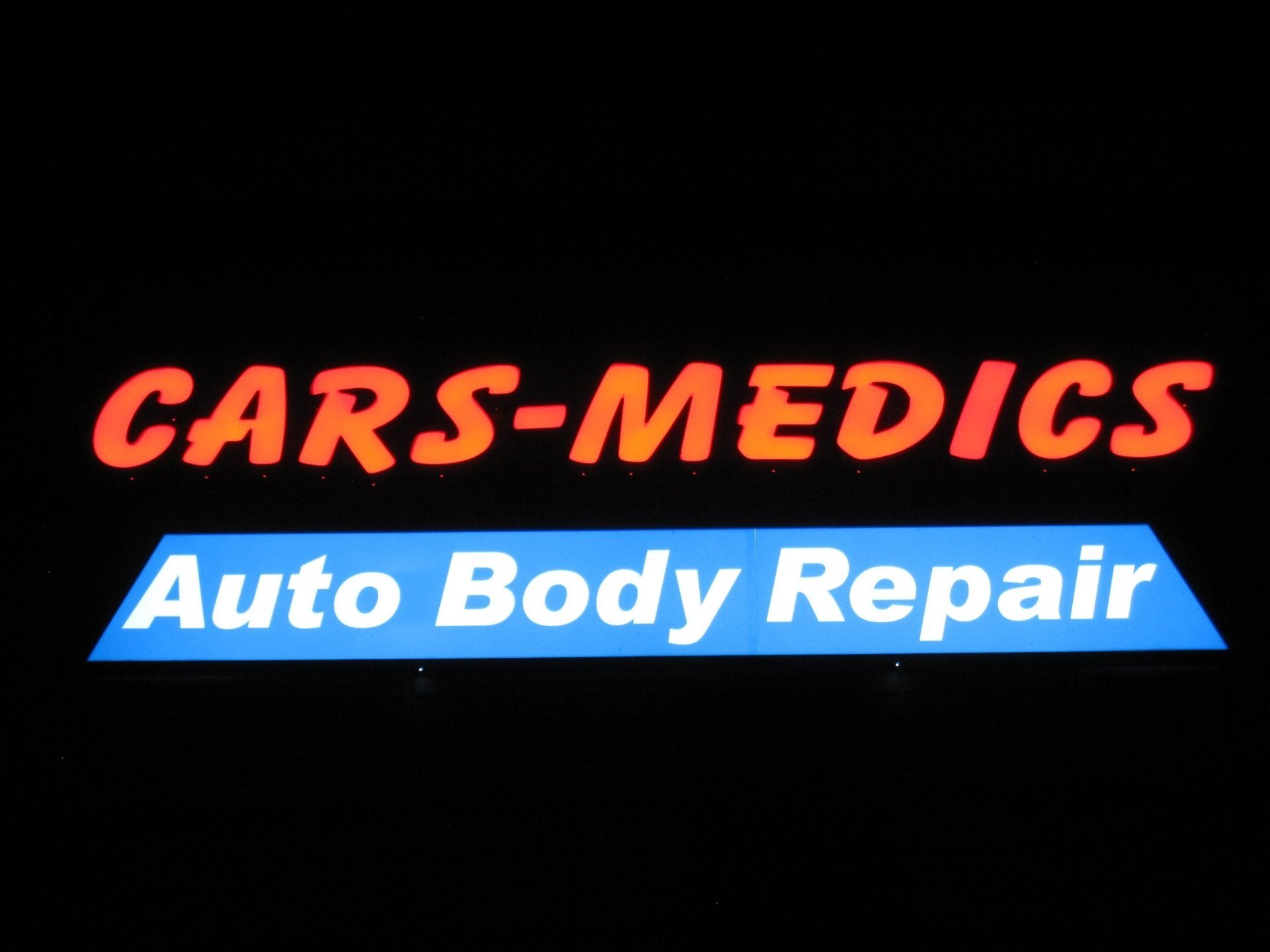 A sign for cars-medics auto body repair is lit up at night