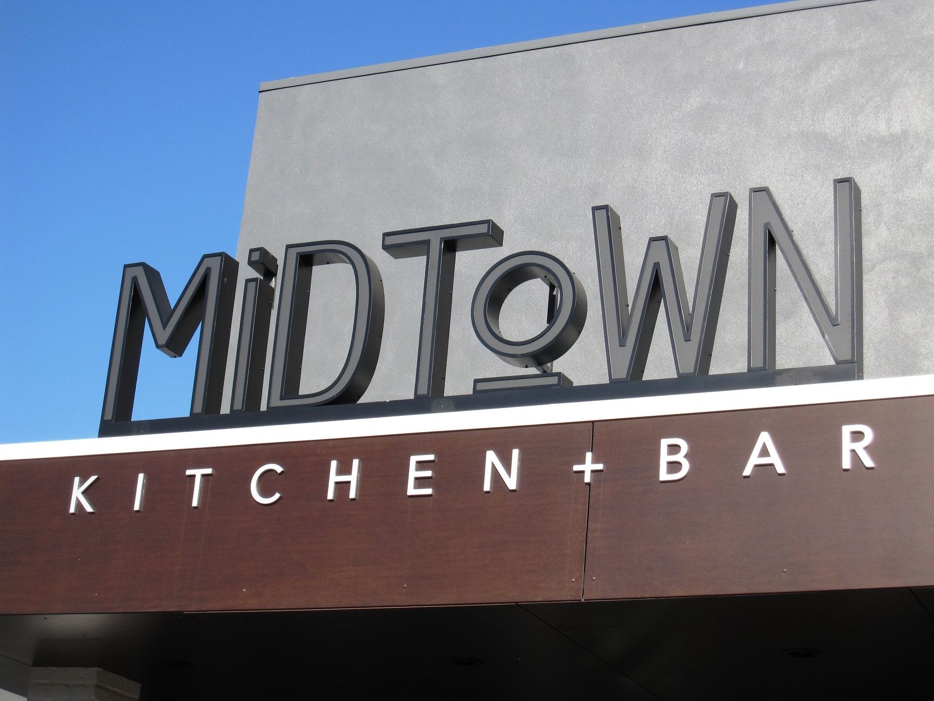 A sign for midtown kitchen and bar with a blue sky in the background