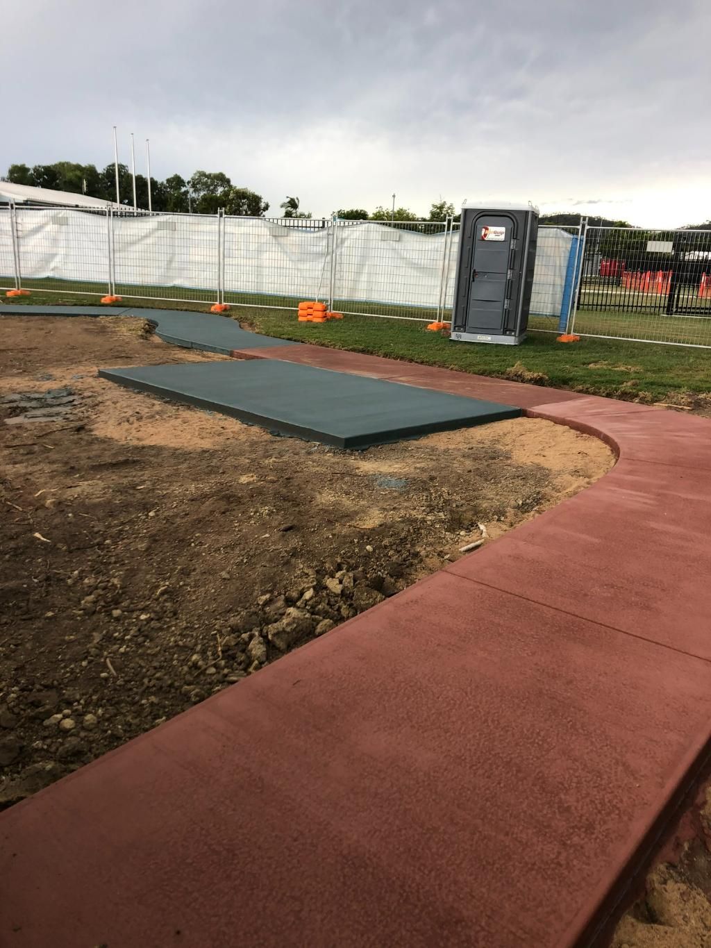 A Portable Toilet Is Sitting in The Middle of A Field Next to A Sidewalk — Fallon Constructions NQ in Fredericksfield, QLD