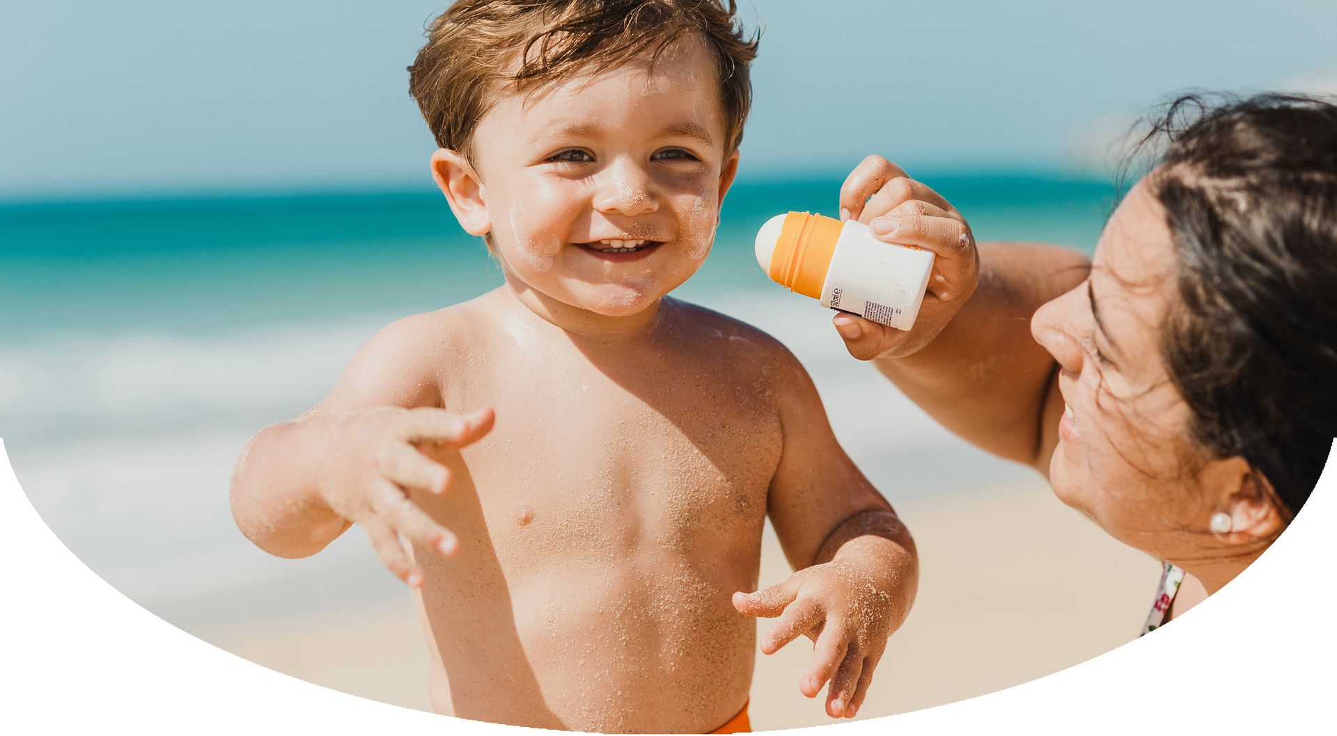 Woman putting sunscreen on boy at the beach