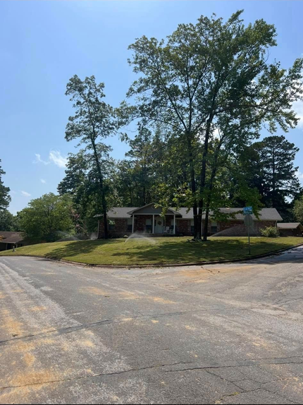 Suburban street corner with a house and tall trees under a clear blue sky