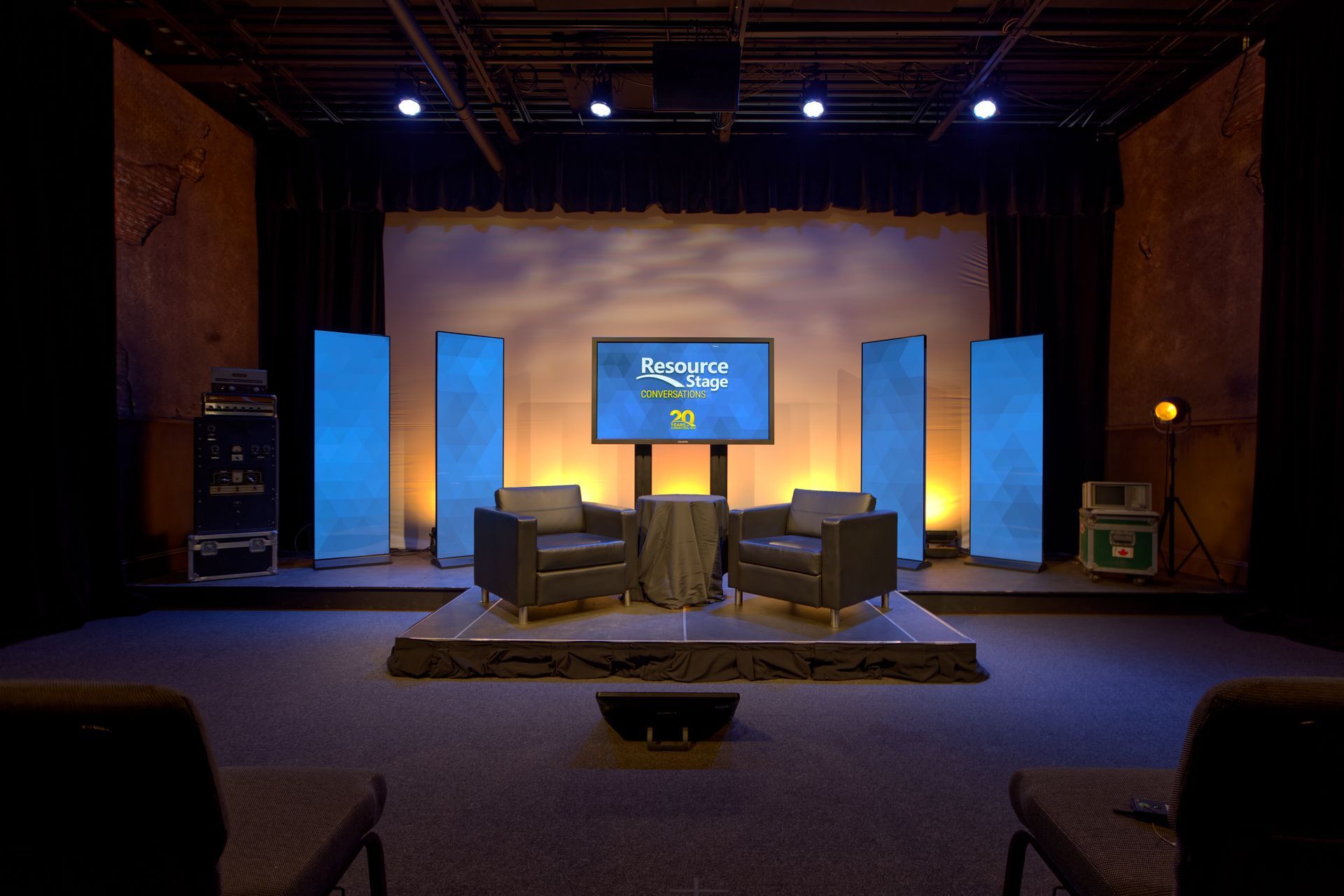 Resource Stage set with two black armchairs facing a screen. Vivid lighting illuminates the backdrop.