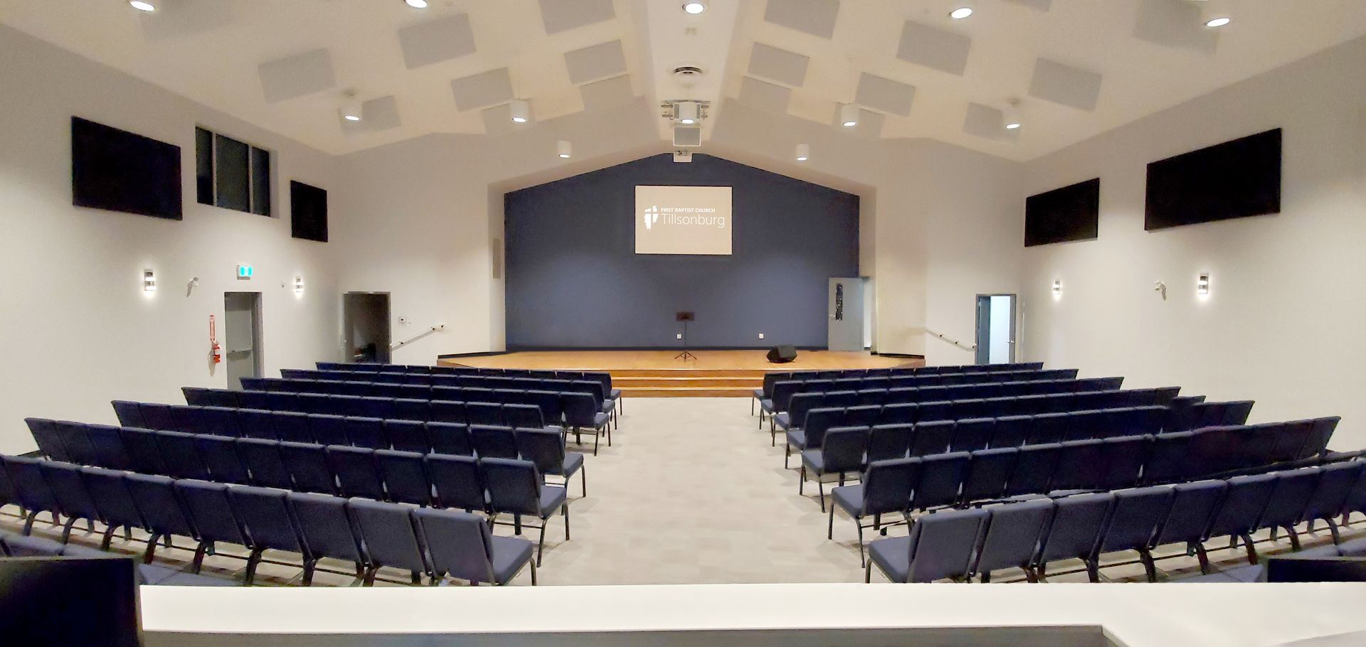 A large auditorium with rows of blue chairs and a stage
