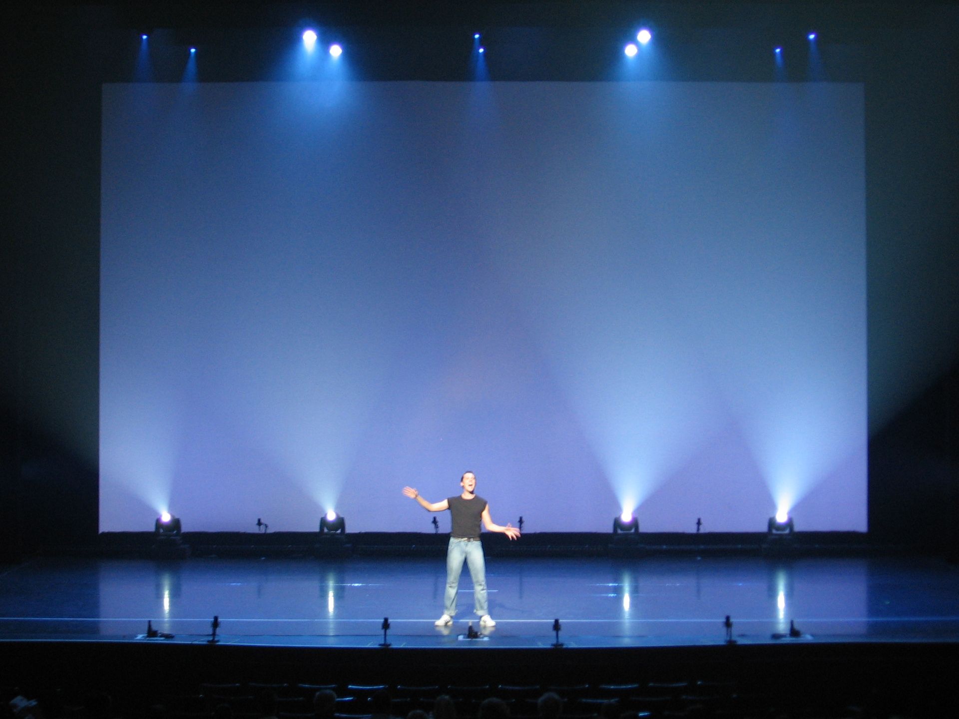 A man is standing on a stage in front of a large screen