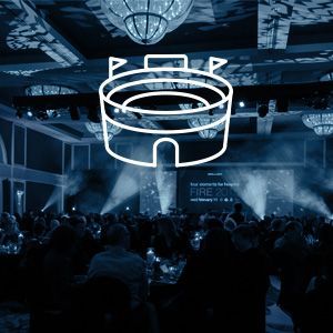 A crowd of people are sitting at tables in a large room with a castle icon on the ceiling.