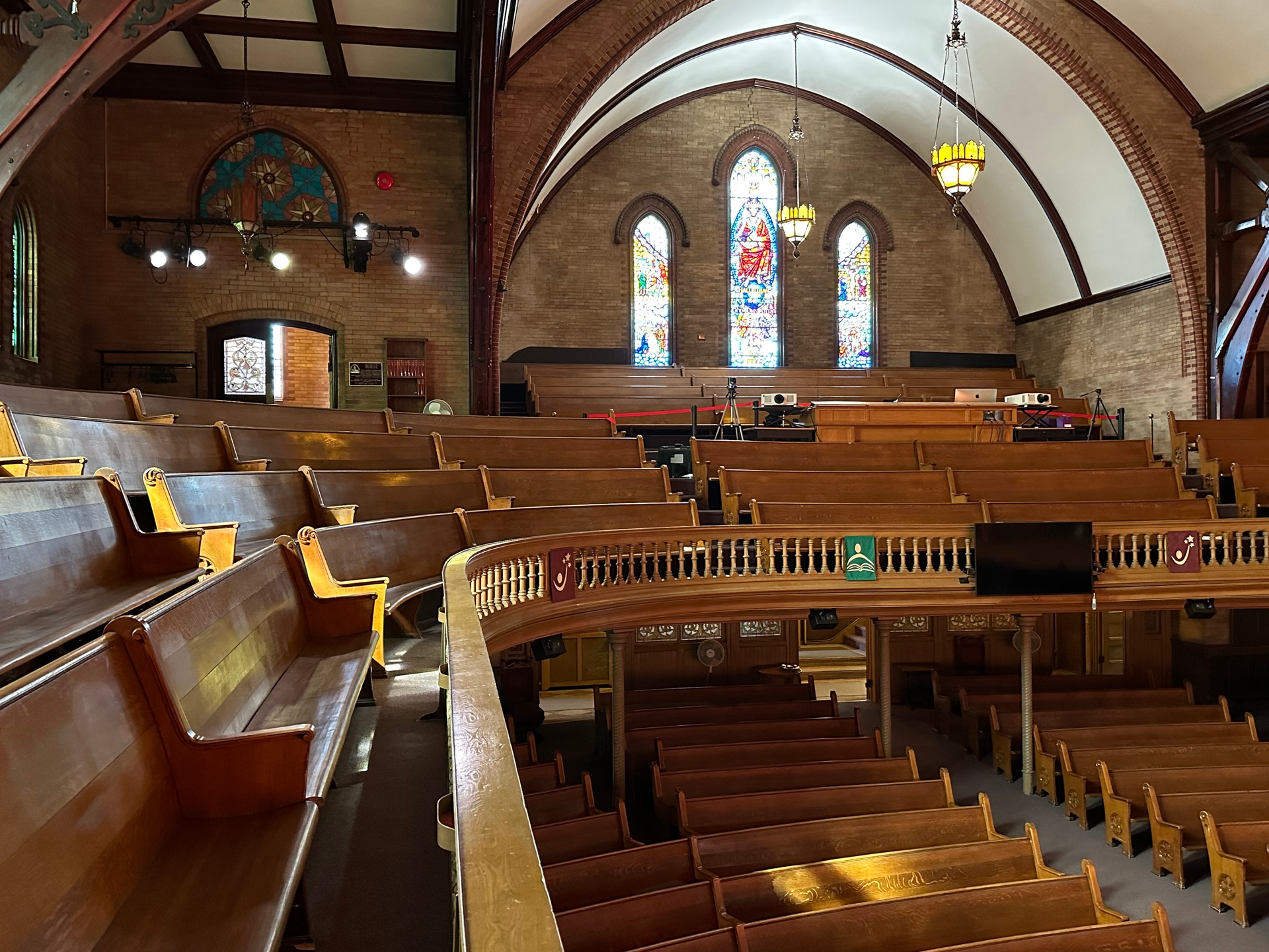 The inside of a church with rows of wooden benches and stained glass windows.