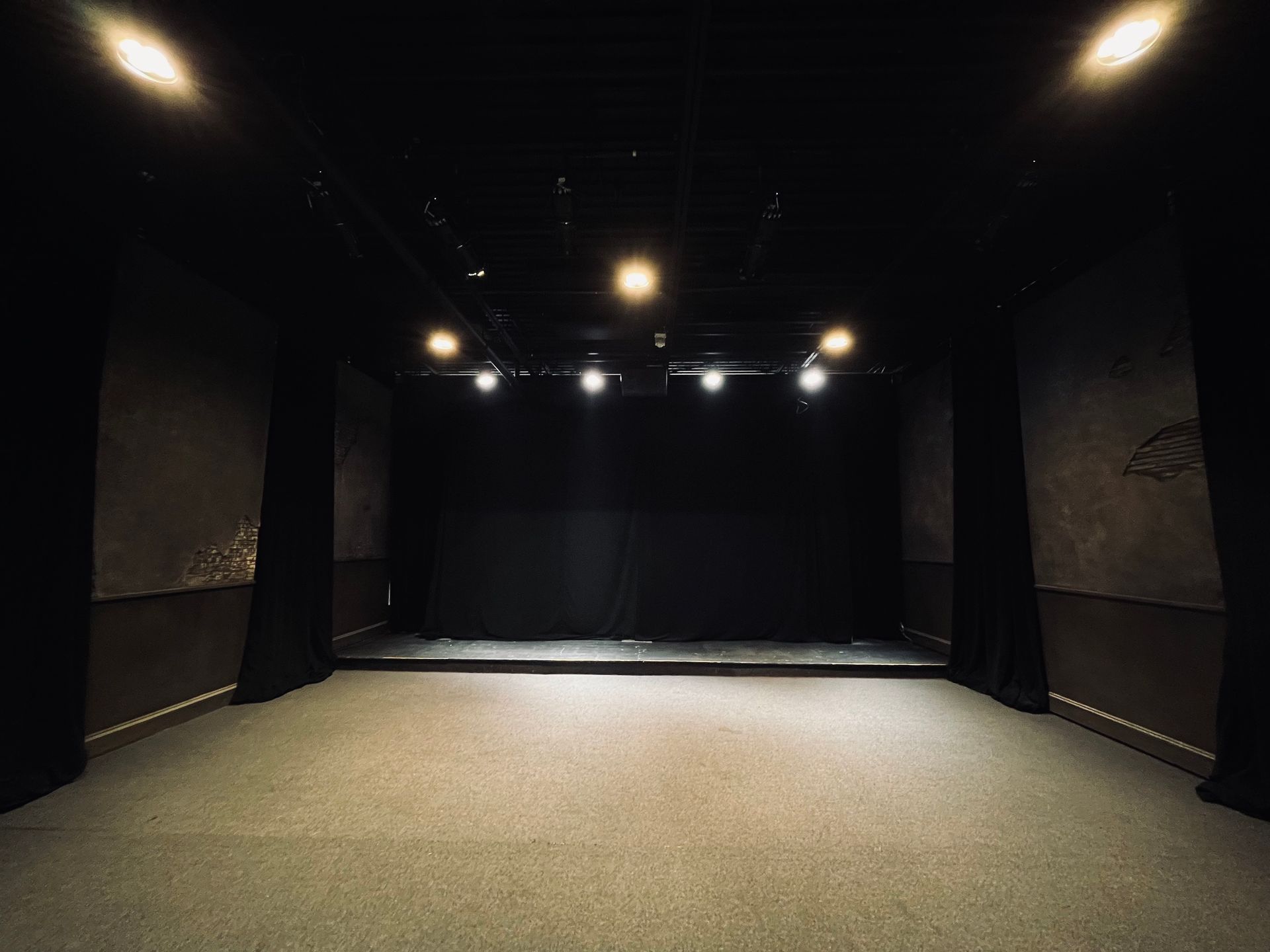 An empty theatre with a black curtain and lights on the stage.