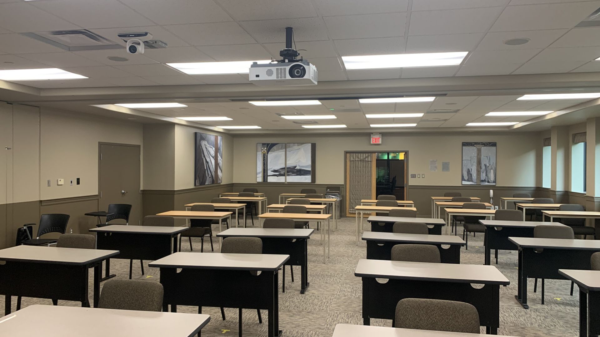 A large classroom with tables and chairs and a projector on the ceiling.
