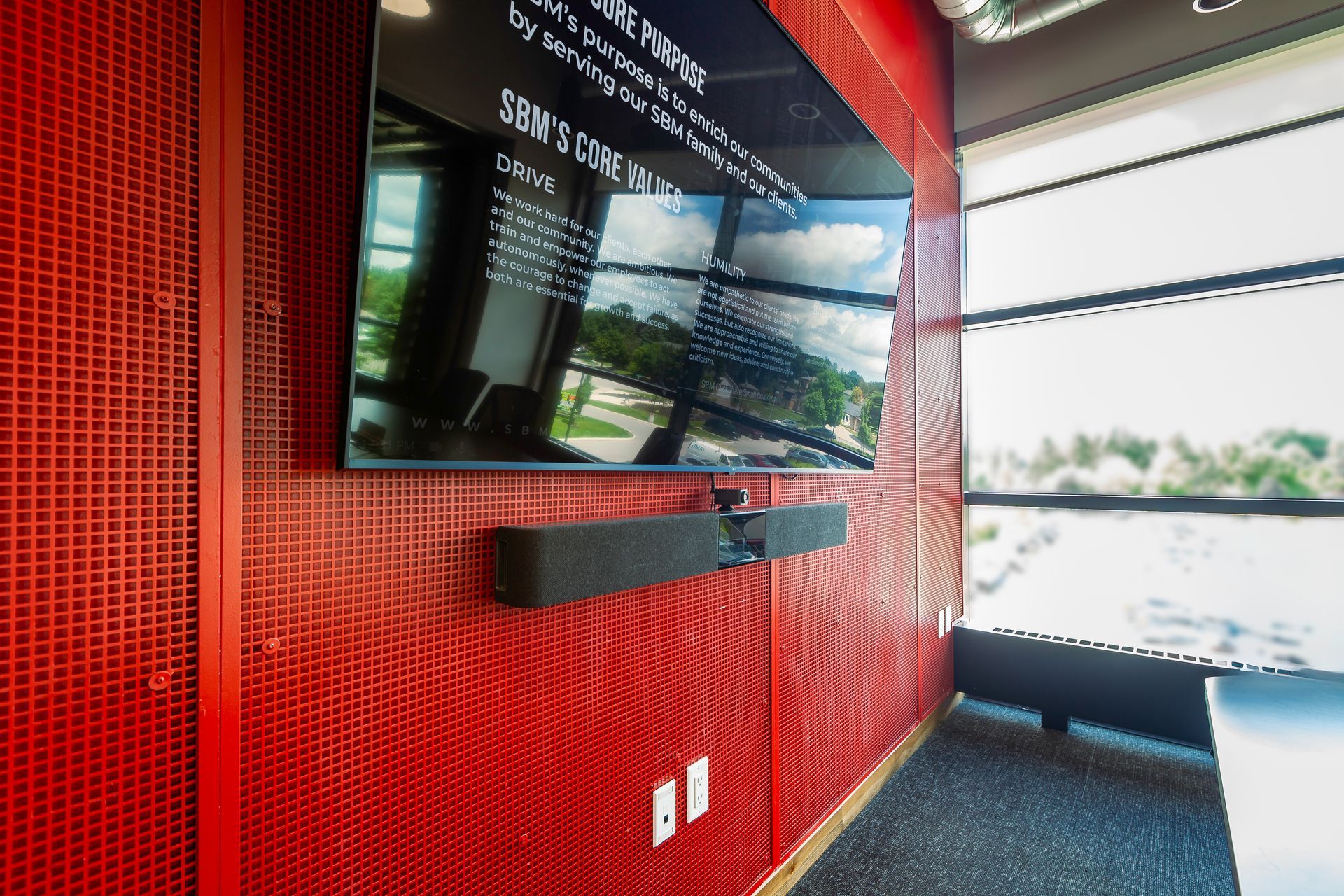 A large flat screen tv is hanging on a red wall with a sound bar installed by Horizon Solutions.