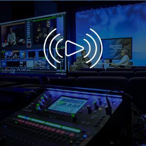 A mixer is sitting in front of a large screen in a dark room.