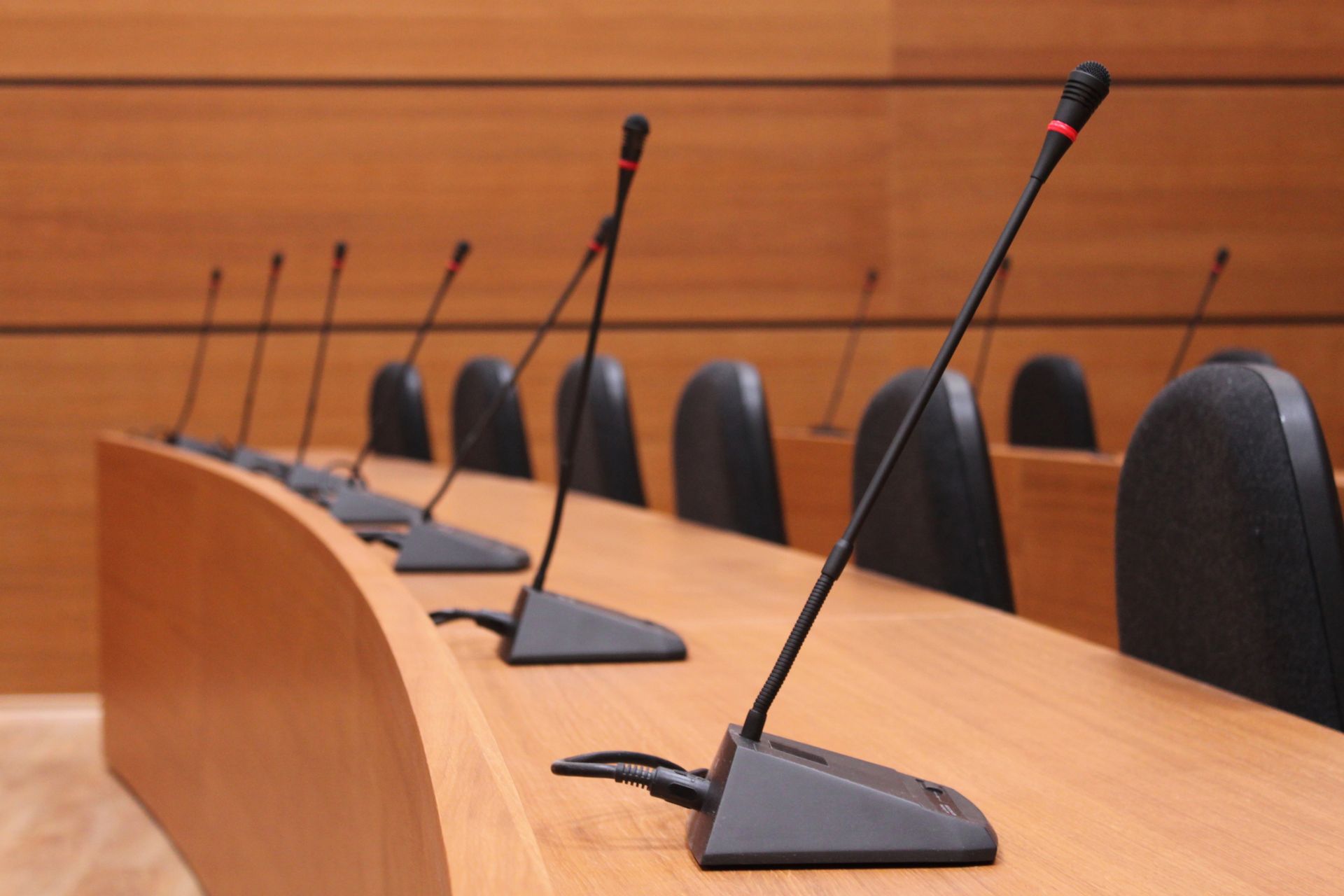 A row of microphones on a wooden table in a conference room