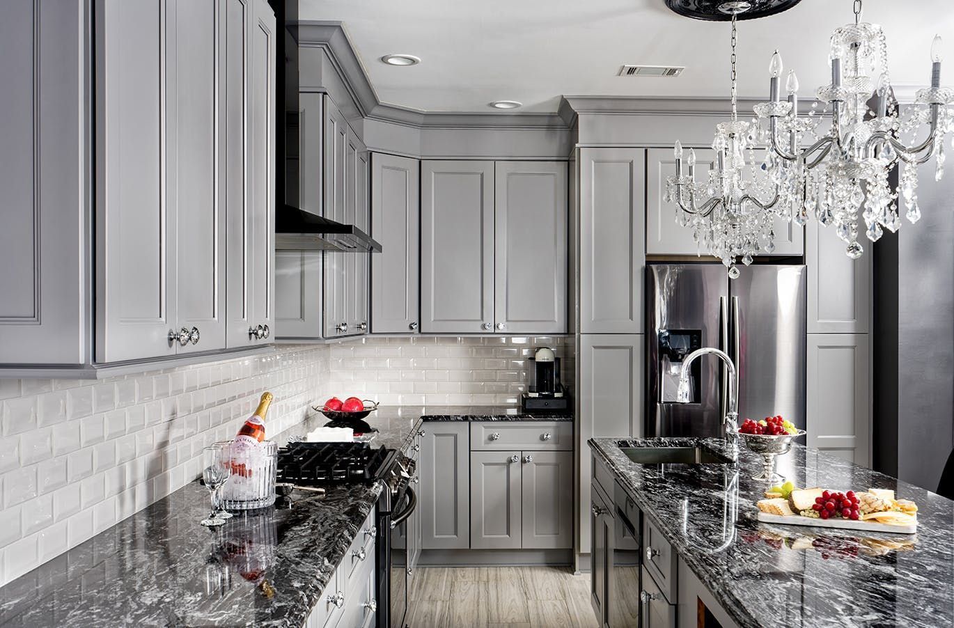 A kitchen with gray cabinets , granite counter tops , stainless steel appliances and a chandelier.