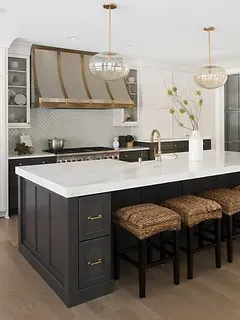 A kitchen with a large island , stools , a sink and a stove.