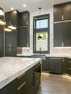 A kitchen with black cabinets , marble counter tops , and a large island.
